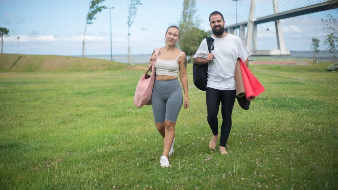 Couple walking in Lisbon park with yoga mats, showcasing active lifestyle in natural setting.